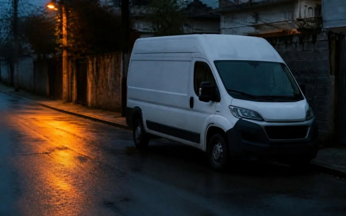 Van de entregas branca estacionada numa rua molhada ao anoitecer